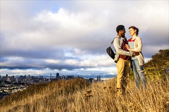 Couple hugging on grassy hill overlooking cityscape