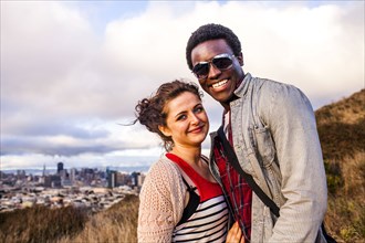 Couple smiling on grassy hill overlooking cityscape