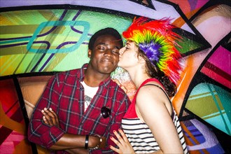 Woman in colorful wig kissing boyfriend near graffiti wall