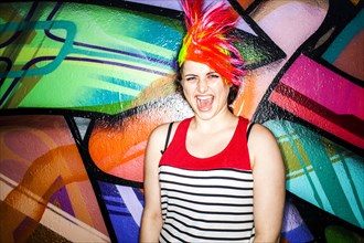 Caucasian woman in colorful wig laughing near graffiti wall
