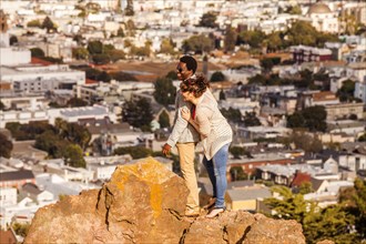 Couple hugging on rock overlooking scenic view of cityscape