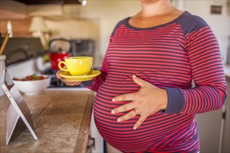 Pregnant Caucasian mother holding cup of tea in kitchen
