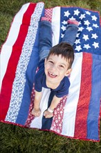 Mixed race boy laying on American flag blanket on grass