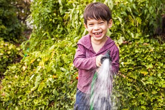 Mixed race boy playing with hose in garden