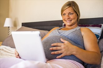 Pregnant Caucasian woman using digital tablet in bed