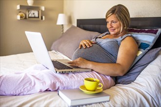 Pregnant Caucasian woman using laptop in bed