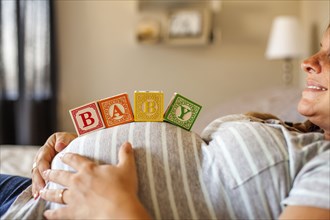Pregnant Caucasian woman balancing wooden blocks on her stomach in bed