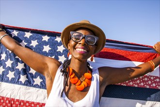 Black woman holding American flag under blue sky