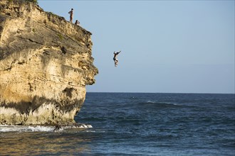 Divers jumping off cliff into ocean