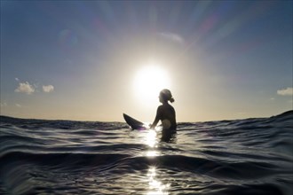 Silhouette of surfer sitting on surfboard in ocean
