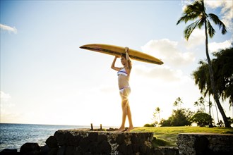Surfer holding surfboard over her head near ocean