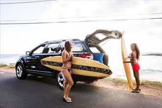 Surfers unloading surfboards from car near beach