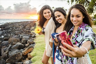 Pacific Islander women taking cell phone photograph near rocky beach