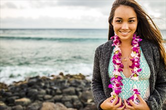 Pacific Islander woman wearing flower lei near rocky beach