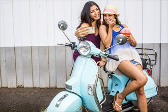 Pacific Islander women taking cell phone photograph on scooter