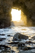 Sunbeam shining through rock formation to ocean waves