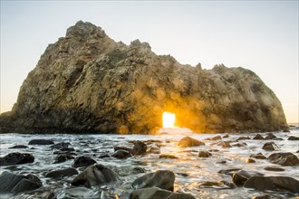 Sun shining through rock formation to ocean waves