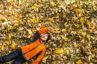 High angle view of mixed race boy laying in autumn leaves