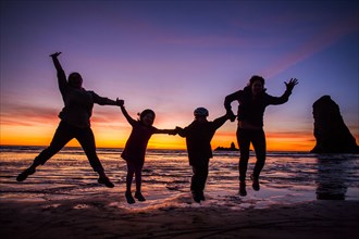 Silhouette of Caucasian family jumping for joy on Cannon Beach