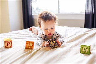 Caucasian baby girl playing with blocks on bed