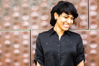 Hispanic woman smiling near metal wall