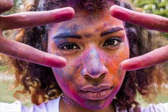 Mixed race woman covered in pigment powder gesturing peace signs