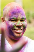 Smiling man covered in pigment powder gesturing peace sign
