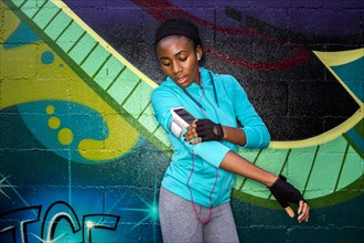 Black runner using cell phone near graffiti wall