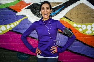 Hispanic runner smiling near graffiti wall