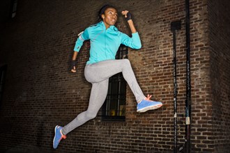 Black woman leaping near brick wall at night