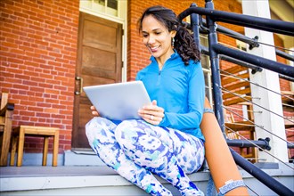 Hispanic woman using digital tablet on porch