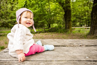 Caucasian baby girl sitting on picnic table in forest
