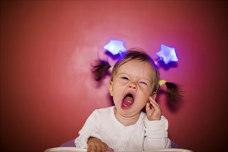 Caucasian baby girl wearing headband with stars and yawning