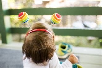 Caucasian baby girl on porch wearing multicolor ball headband