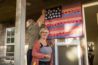 Caucasian couple hanging homemade American flag on porch