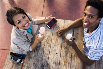 Couple eating ice cream and using cell phone at picnic table