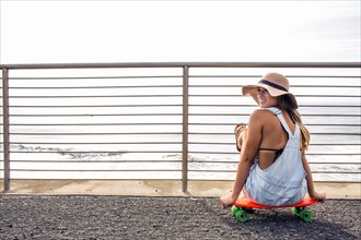 Caucasian woman sitting on skateboard at beach