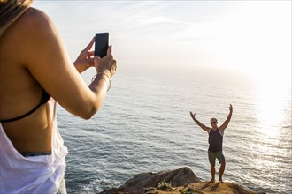 Caucasian man photographing girlfriend on cliff