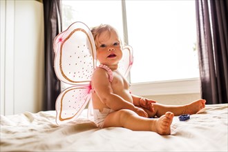 Caucasian baby girl wearing fairy wings on bed