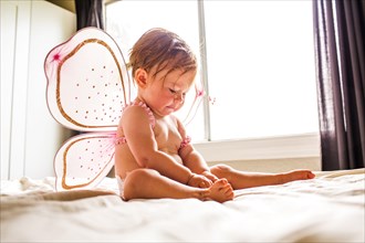 Caucasian baby girl wearing fairy wings on bed