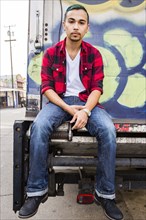 Hispanic man sitting on graffiti truck