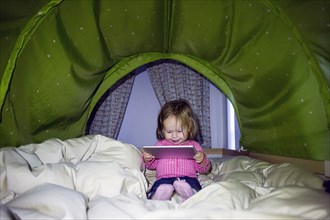 Caucasian baby girl using digital tablet in tent