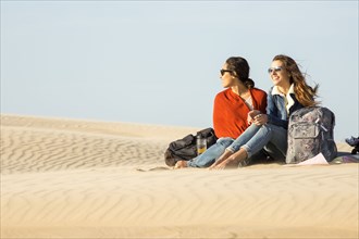 Mixed race women sitting in sand dunes
