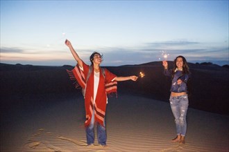 Mixed race women playing with sparklers on sand dunes