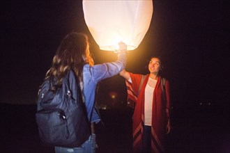 Mixed race women floating lantern at night