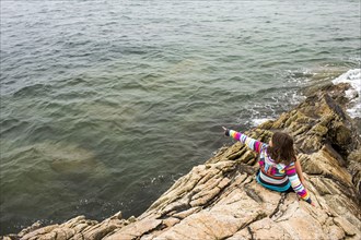 Caucasian girl sitting on rocks pointing at ocean