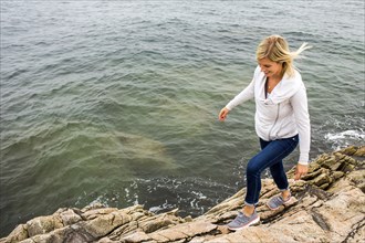 Caucasian woman walking on rocks at ocean