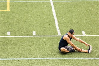 Caucasian man sitting on sports field stretching leg