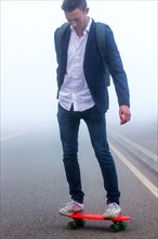 Caucasian man standing on small red skateboard in fog