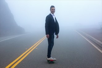 Caucasian man standing on small red skateboard in fog